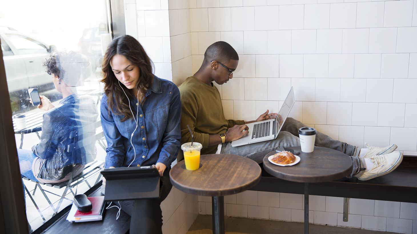 En tjej och en kille sitter med varsin laptop i en restaurangmiljö 