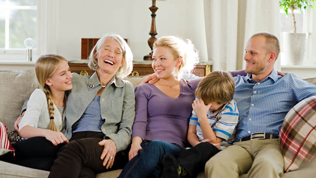 Ett vardagsrum, flera generationer skrattar tillsammans i en soffa