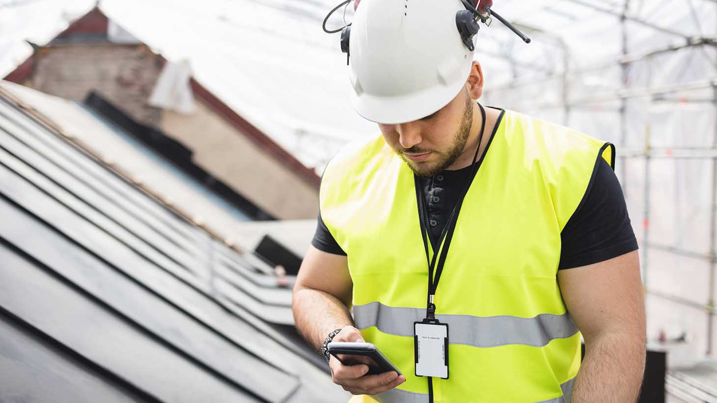 En byggnadsarbetare står på ett tak och kollar sin mobiltelefon