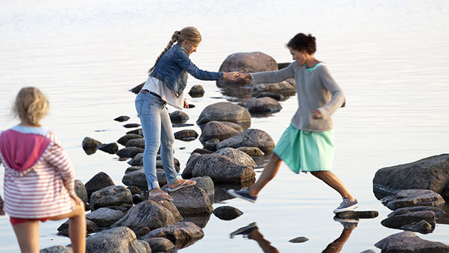 En mamma med barn hoppar över stenar vid en strand