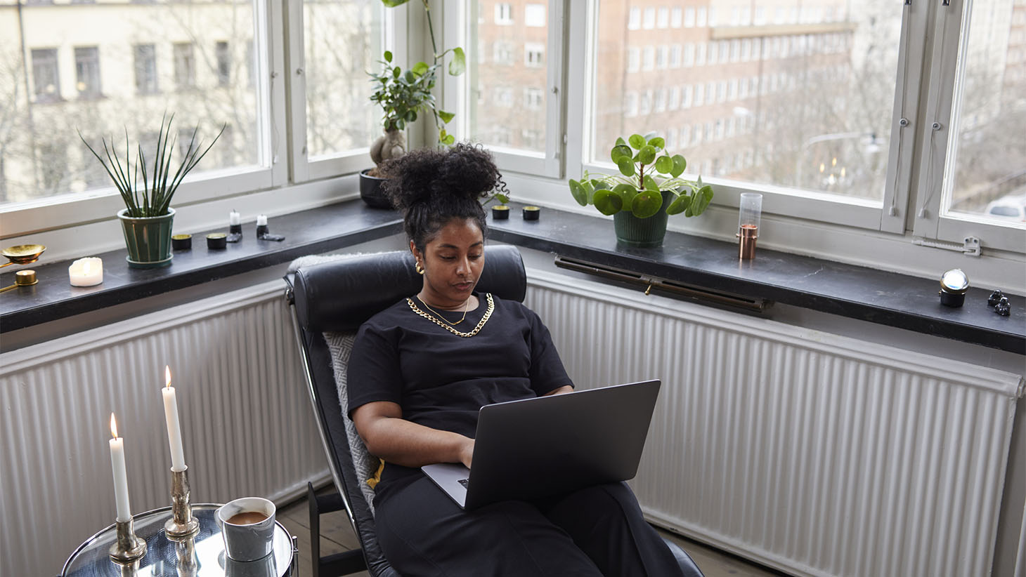 En kvinna sitter i en fåtölj hemma och jobbar på datorn