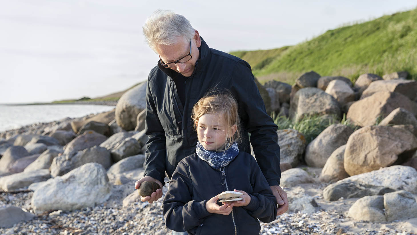 En man och en flicka letar stenar på en strand.