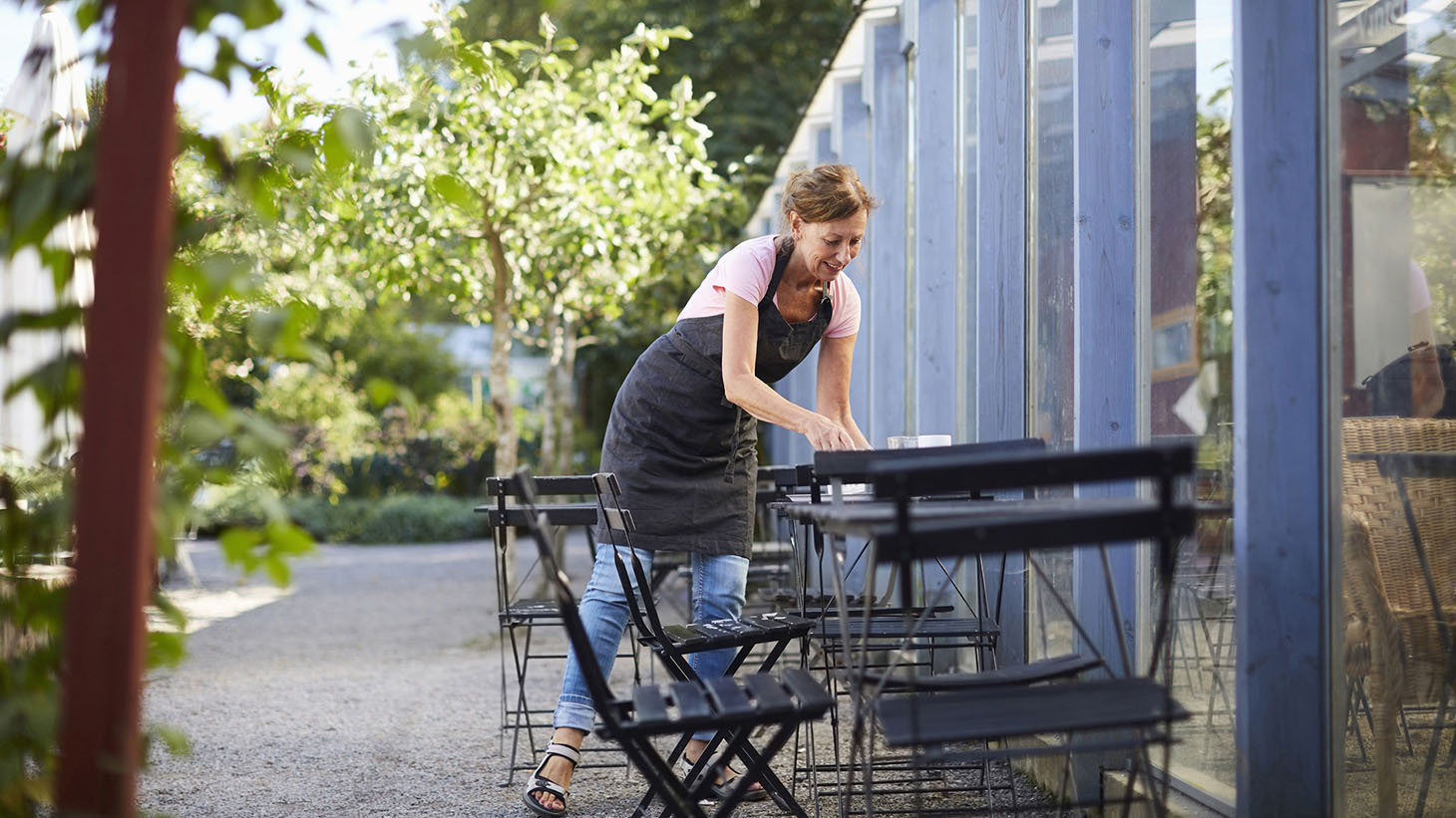En kvinna torkar av cafébord utanför ett växthus