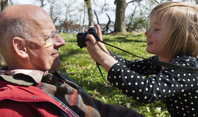 En morfar/farfar och ett barnbarn leker med en kamera