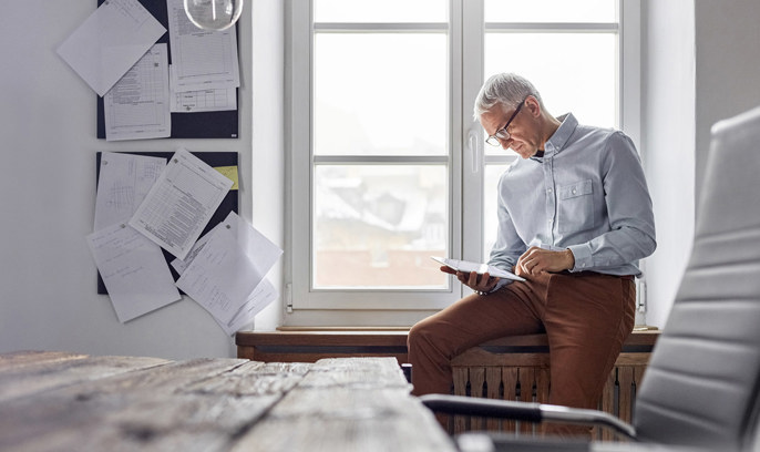En man sitter i ett fönster och tittar på en surfplatta