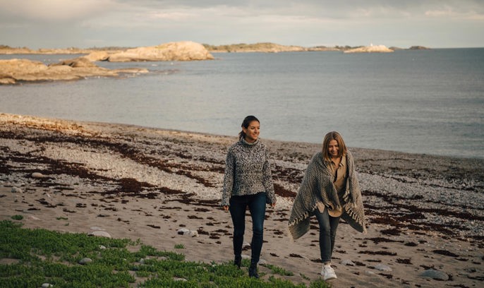 Unga kvinnor går på en strand i skymningen.