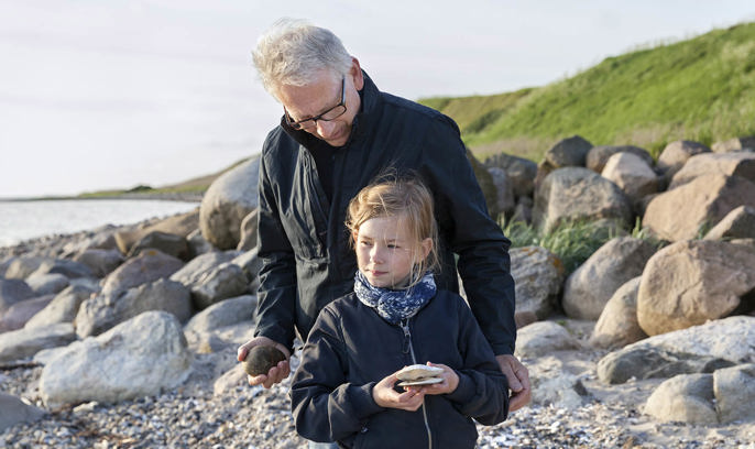 En man och en flicka letar stenar på en strand.