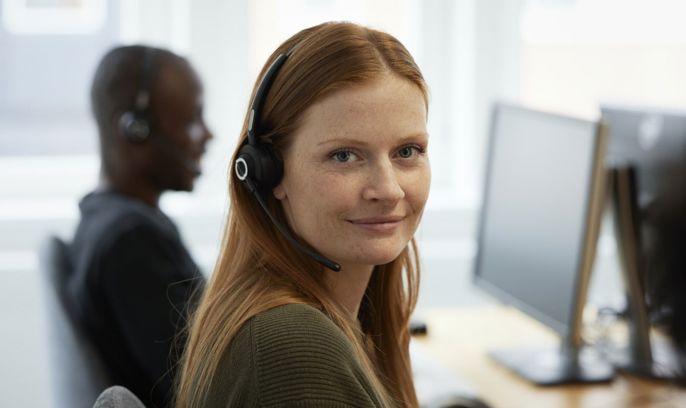 En ung kvinna sitter med headset i en kundservice