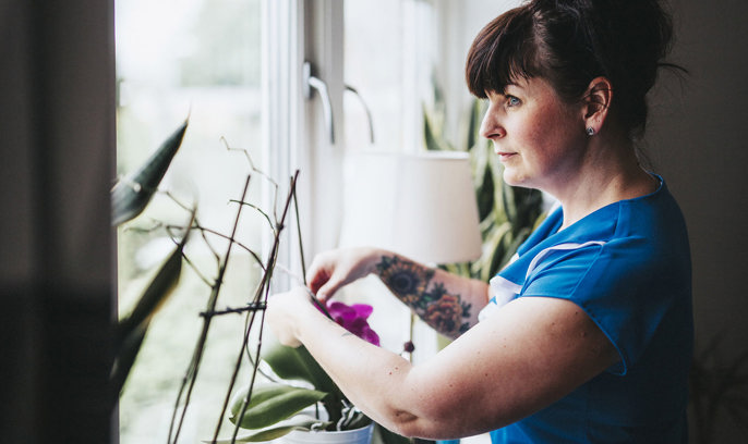 En kvinna tar hand om en blomma och tittar ut genom fönstret