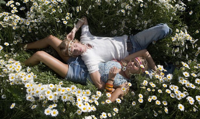 Ett ungt par ligger bredvid varandra på ett sommaräng med prästkragar